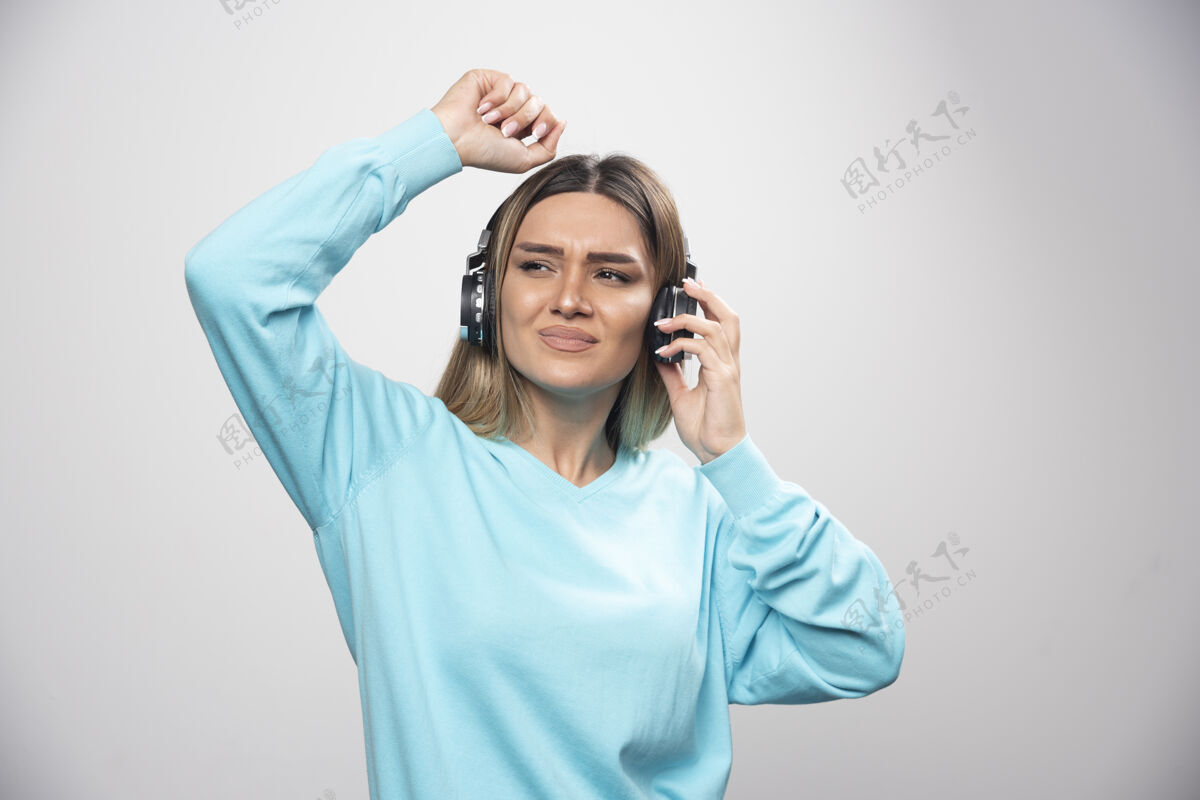 成人穿着蓝色运动衫的金发女孩戴着耳机 享受着音乐和乐趣积极人类积极