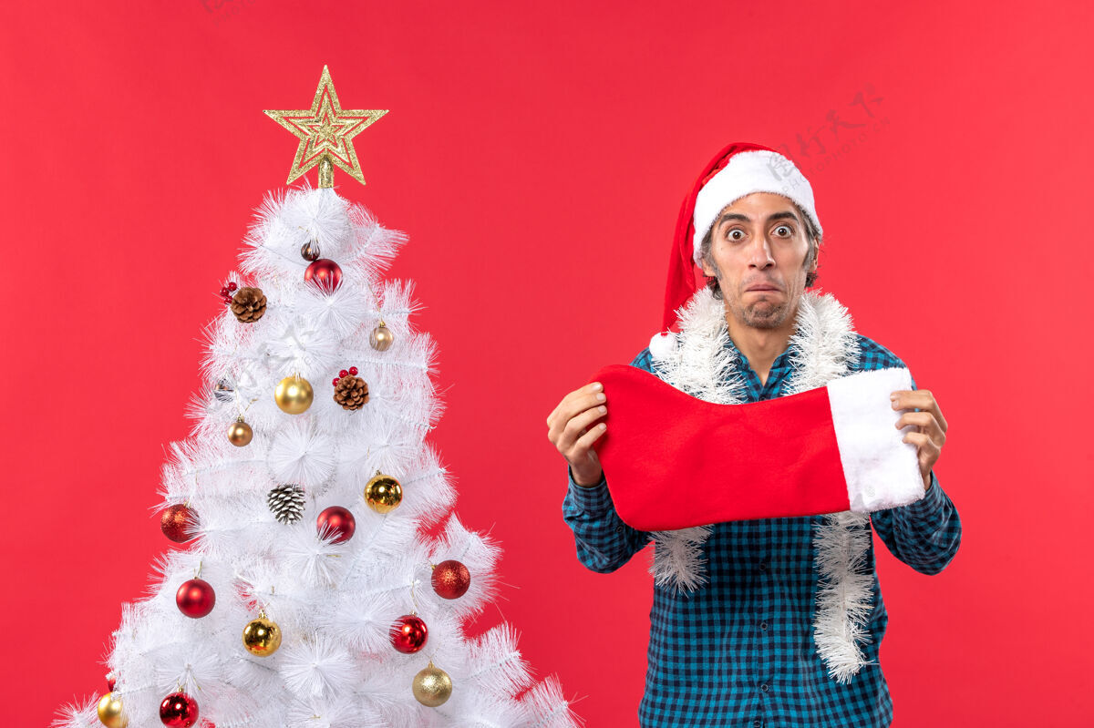 帽子情绪低落的年轻人戴着圣诞老人的帽子 穿着蓝色的衬衫 手里拿着圣诞袜子服装圣诞老人衬衫