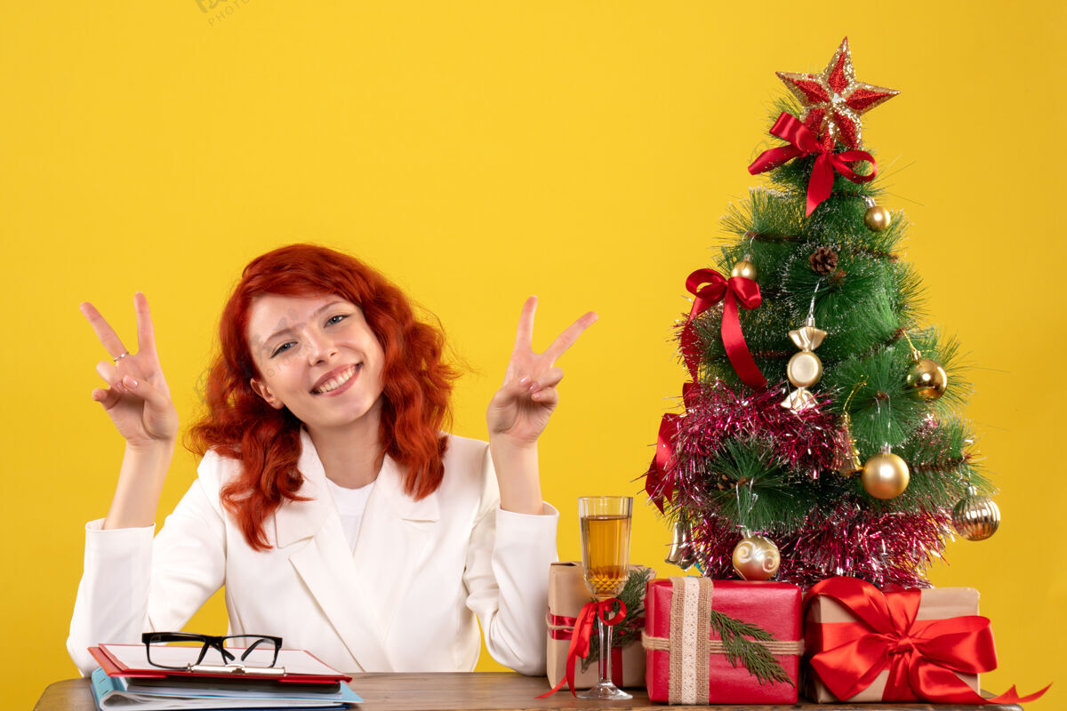 黄色女工人坐在桌子后面 手里拿着圣诞礼物和黄色的圣诞树树桌子情感