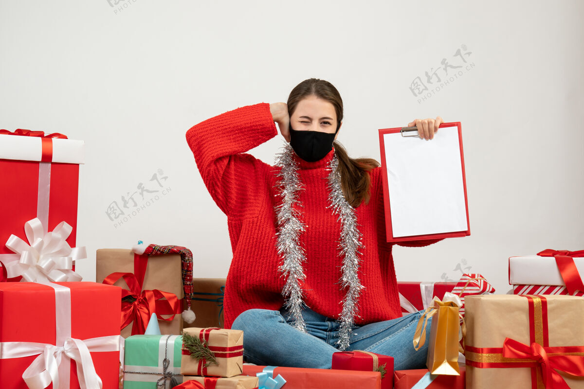 礼物戴着黑色面具的年轻女孩拿着文件捂着耳朵坐在白色的礼物旁边周围女孩礼物