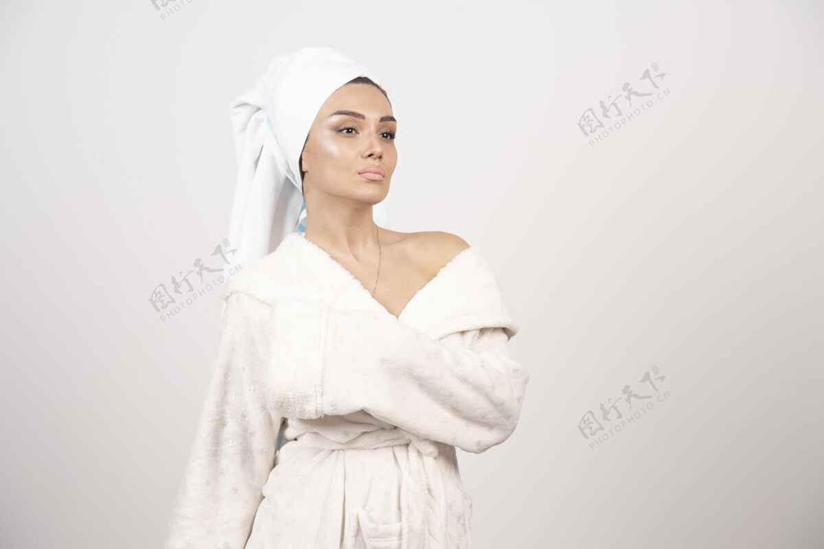 人穿着白色浴袍的漂亮年轻女子在白墙上摆姿势头毛巾治疗