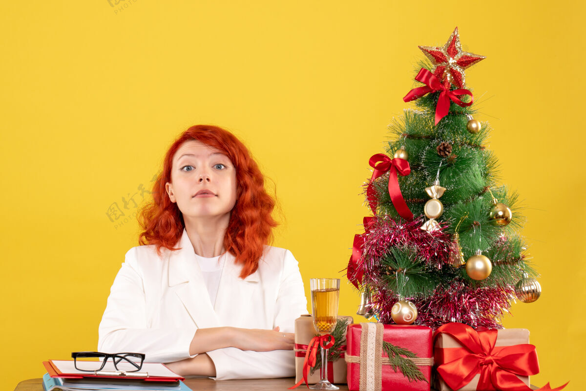 家前视图：女医生坐在桌子后面 黄色背景上有圣诞礼物安排女性背景