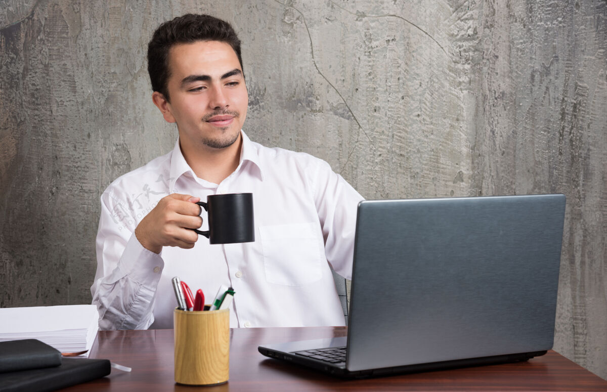 员工商人端着一杯茶 看着办公桌上的笔记本电脑人茶喝酒