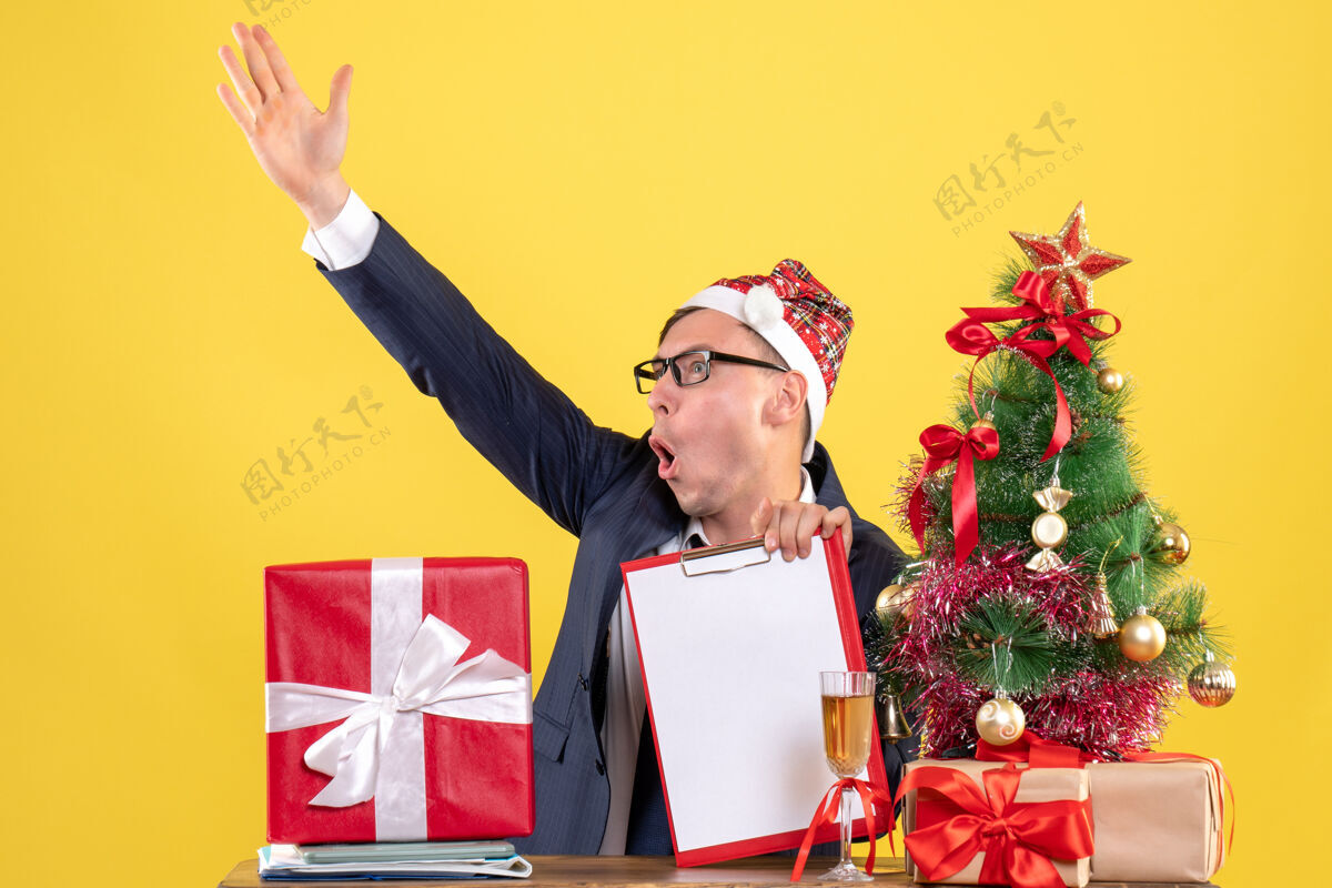 圣诞节前视图：商人对着坐在圣诞树旁的桌子上的人大喊大叫 黄色的礼物男人人商人