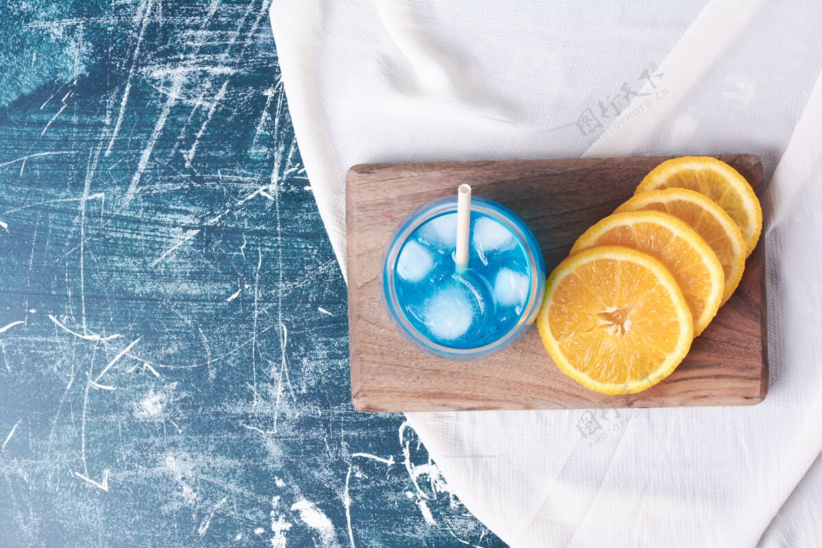 水橘子片加一杯果汁放在蓝色上饮料点心鸡尾酒