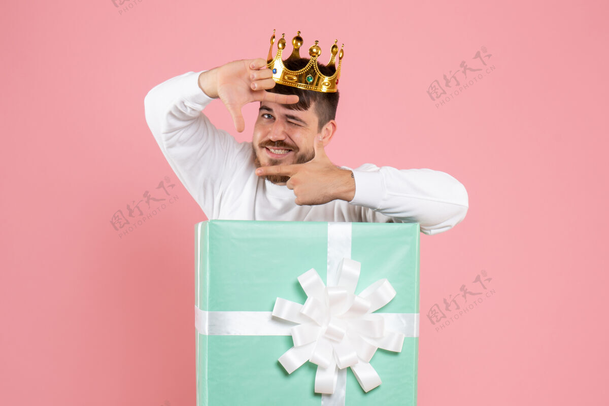 聚会年轻人在礼物盒内的正面视图 粉红色墙上有皇冠粉色成人人物