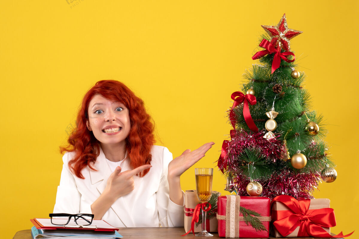 情感女工人坐在桌子后面 手里拿着圣诞礼物和黄色的圣诞树办公室安排树