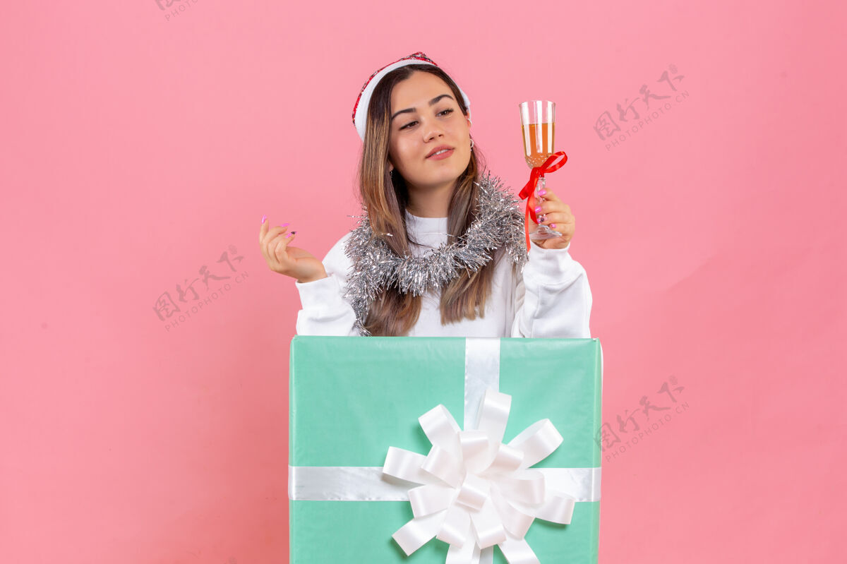 礼物前视图的年轻女子庆祝圣诞节与饮料上粉红色的墙壁年轻女性礼物