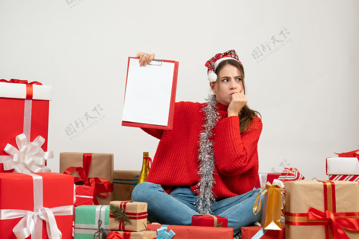 人们带着圣诞帽的体贴女孩拿着文件围坐在白色的礼物上体贴的女孩周围女孩