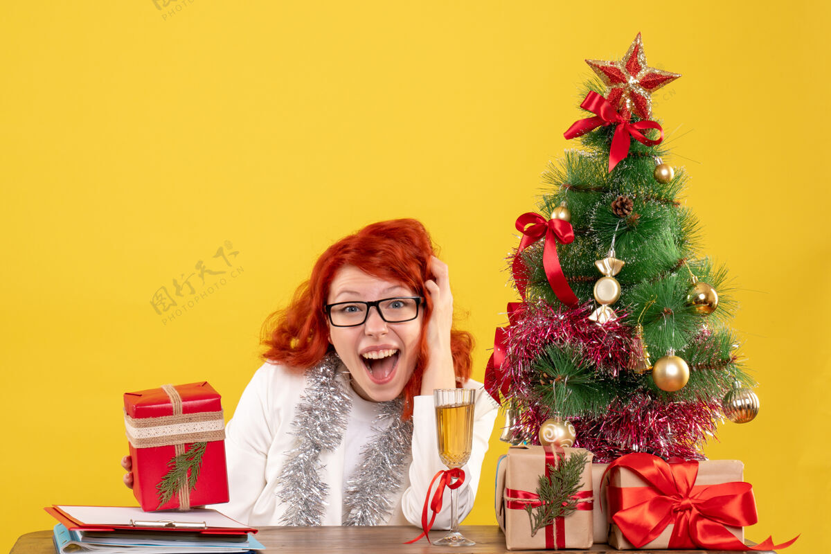 花前视图：女医生坐在桌子后面 黄色背景上有圣诞礼物情感庆祝插花