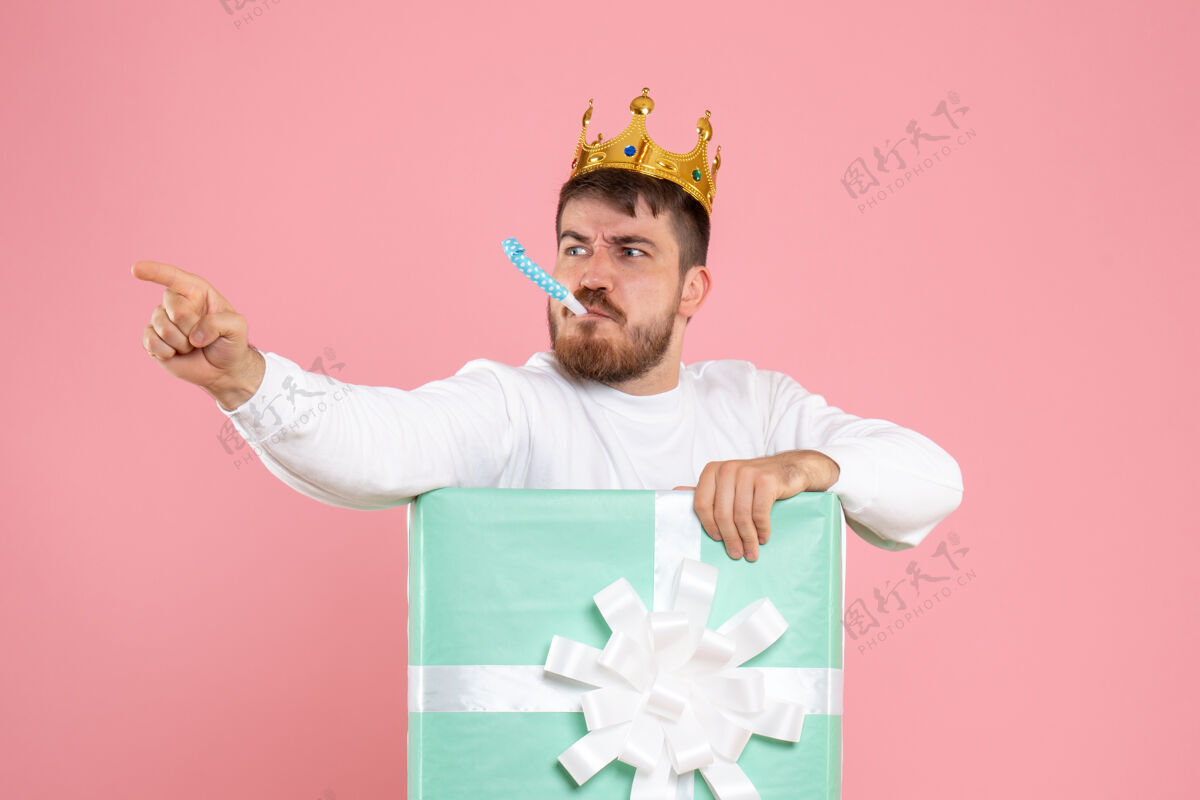 礼物粉红色墙上戴着王冠的礼物盒内年轻人的正面图盒子粉色男人
