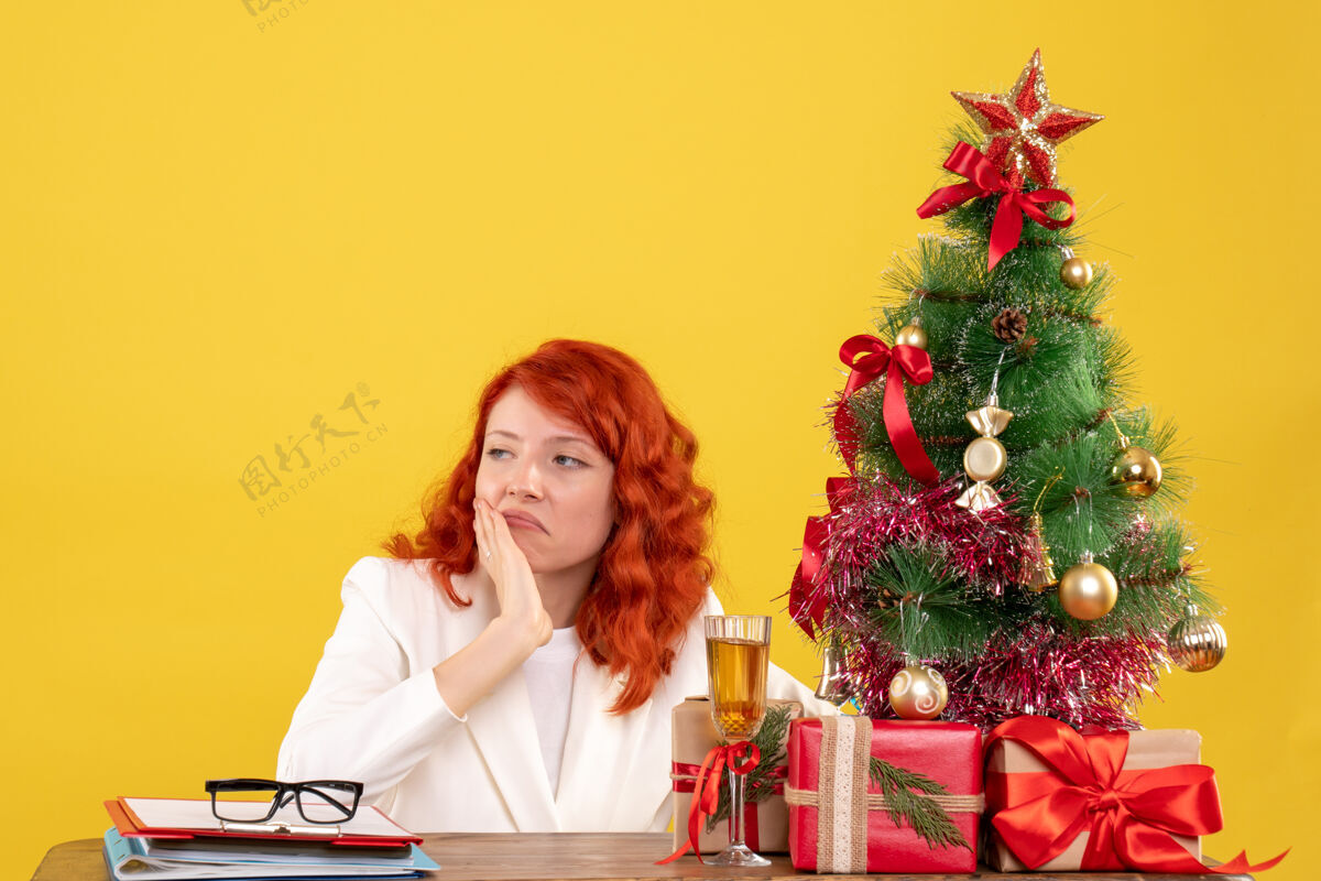 礼物前视图：女医生坐在桌子后面 黄色背景上有圣诞礼物花坐安排