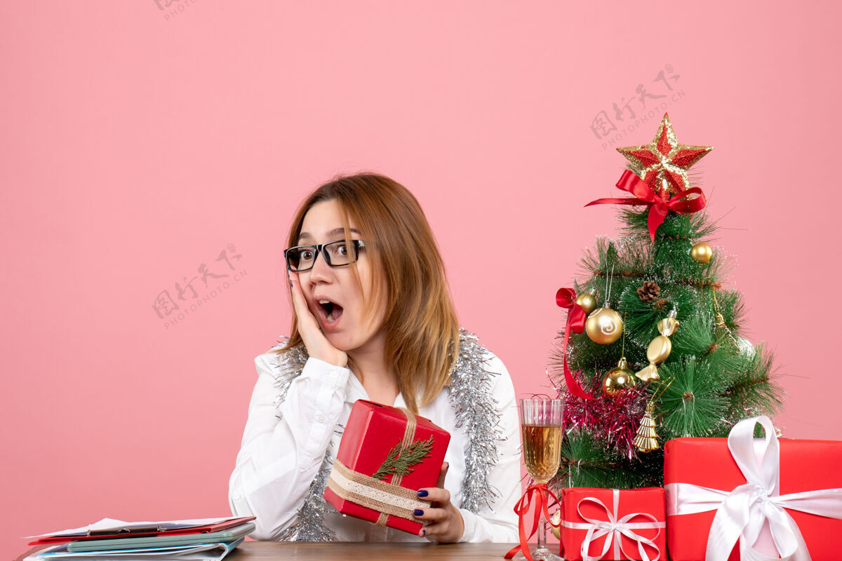 礼物女工人坐在粉红色的圣诞礼物和圣诞树旁的正视图人工作粉红色