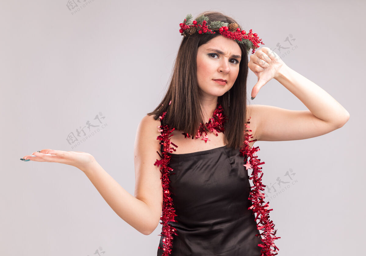 漂亮一个年轻漂亮的白人女孩戴着圣诞花环 脖子上戴着金属丝花环 空着手 拇指朝下 看着隔离在白色背景上的相机头未发布手