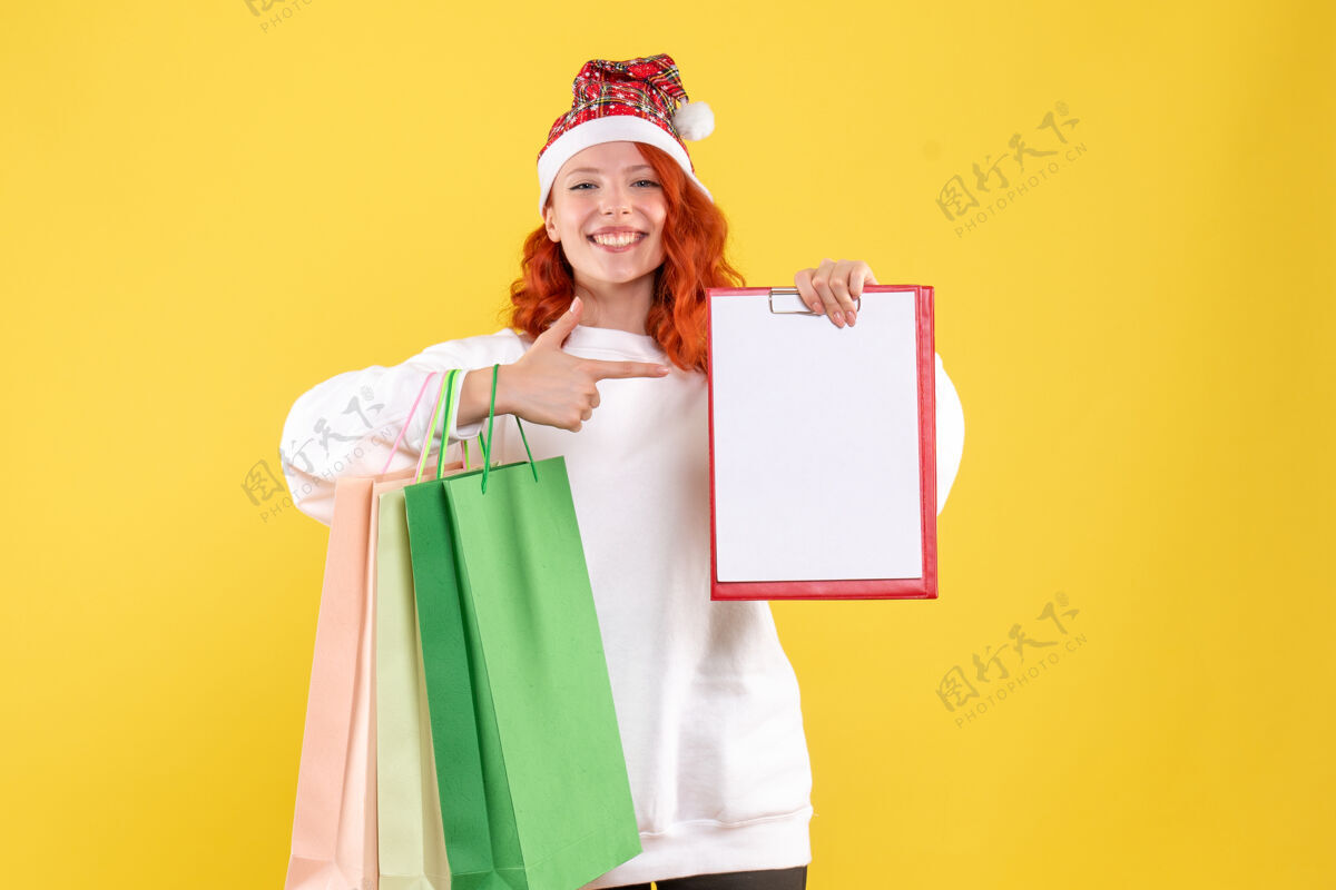抱着黄色墙壁上拿着购物包的年轻女子的正视图圣诞节漂亮人