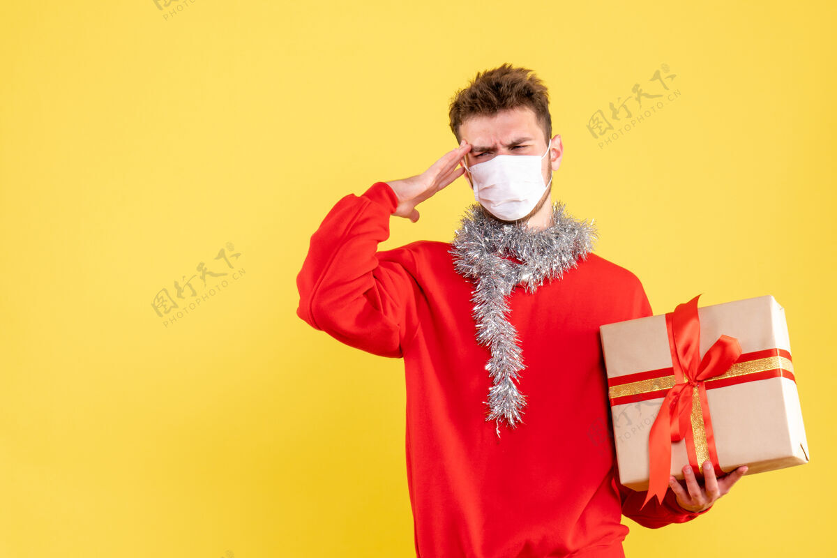 年轻男性正面图：戴着无菌面具的年轻男性手持圣诞礼物漂亮面具礼物