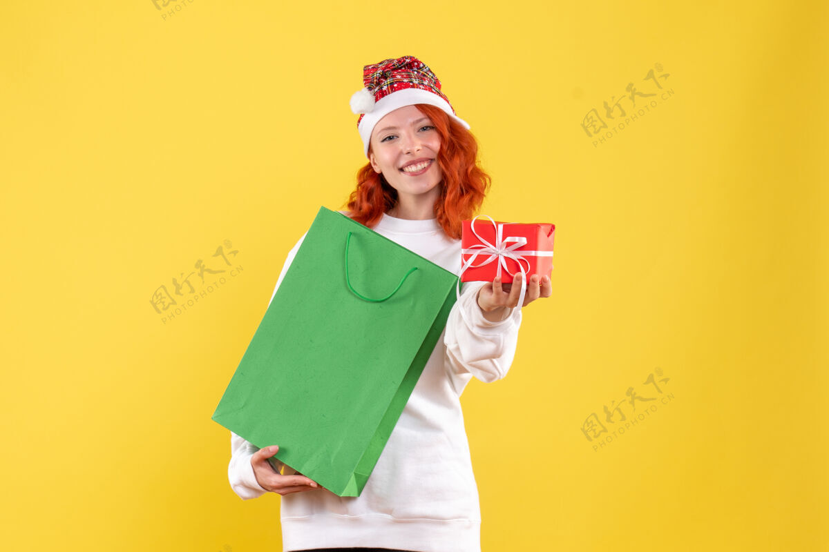 肖像黄色墙上拿着包裹和小礼物的年轻女子的正视图帽子人女人