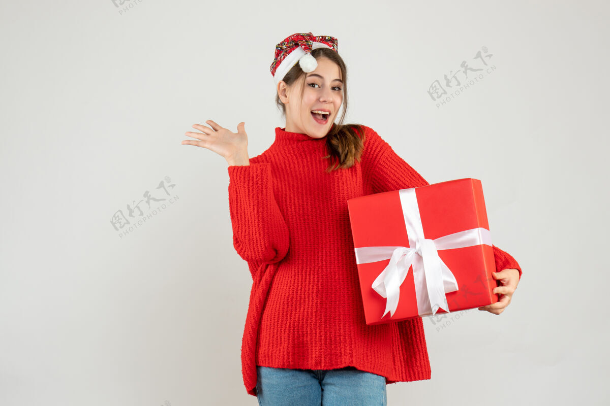 圣诞老人戴着圣诞帽的快乐女孩拿着礼物盒站在白色的地板上礼物快乐圣诞节