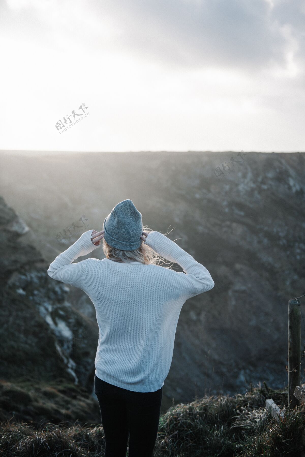 山脉年轻的金发女郎戴着帽子 在多风的天气里走在多岩石的海岸上雾女人年轻