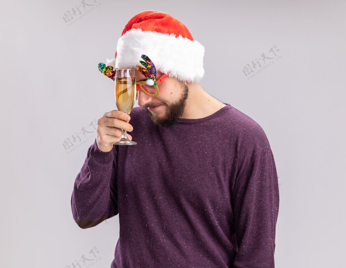 无聊穿着紫色毛衣 戴着圣诞帽的年轻人戴着滑稽的眼镜 手里拿着一杯香槟 站在白色的背景下显得又累又无聊眼镜抱着香槟