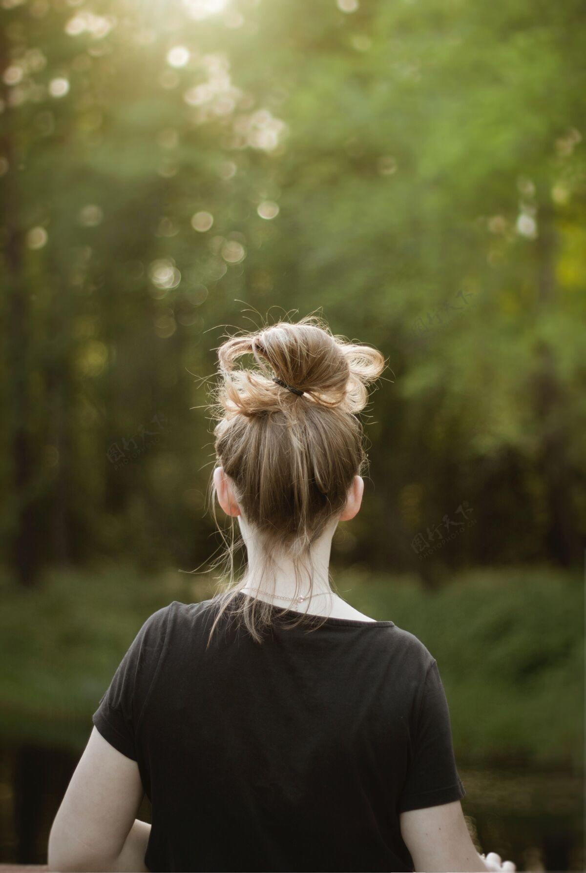 自然一个穿着黑色衬衫的年轻金发女性看着美丽的绿色植物的垂直镜头背景看起来草