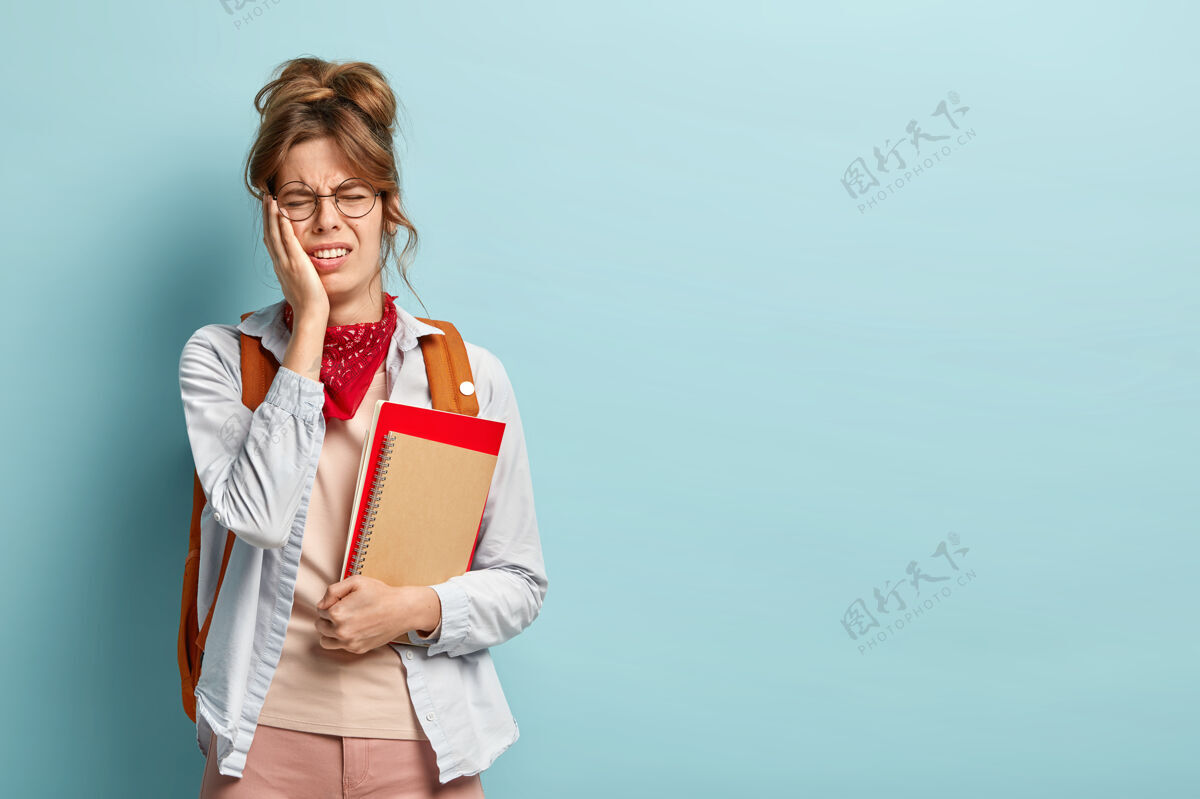 墙壁不满紧张疲惫的女生照片拿着螺旋记事本和书 戴着圆眼镜沮丧失望学生