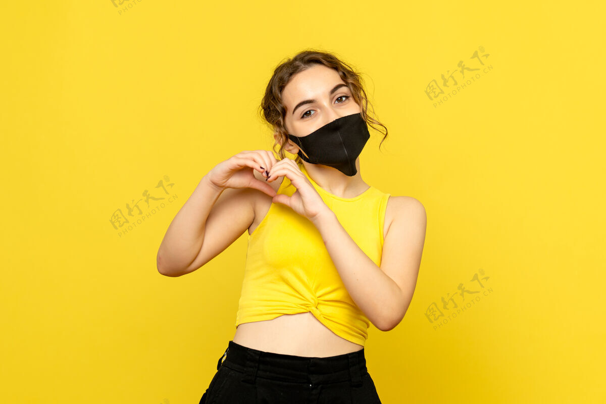 时尚戴着面具的年轻女子在黄色墙壁上传递爱的正面图年轻面具年轻女性