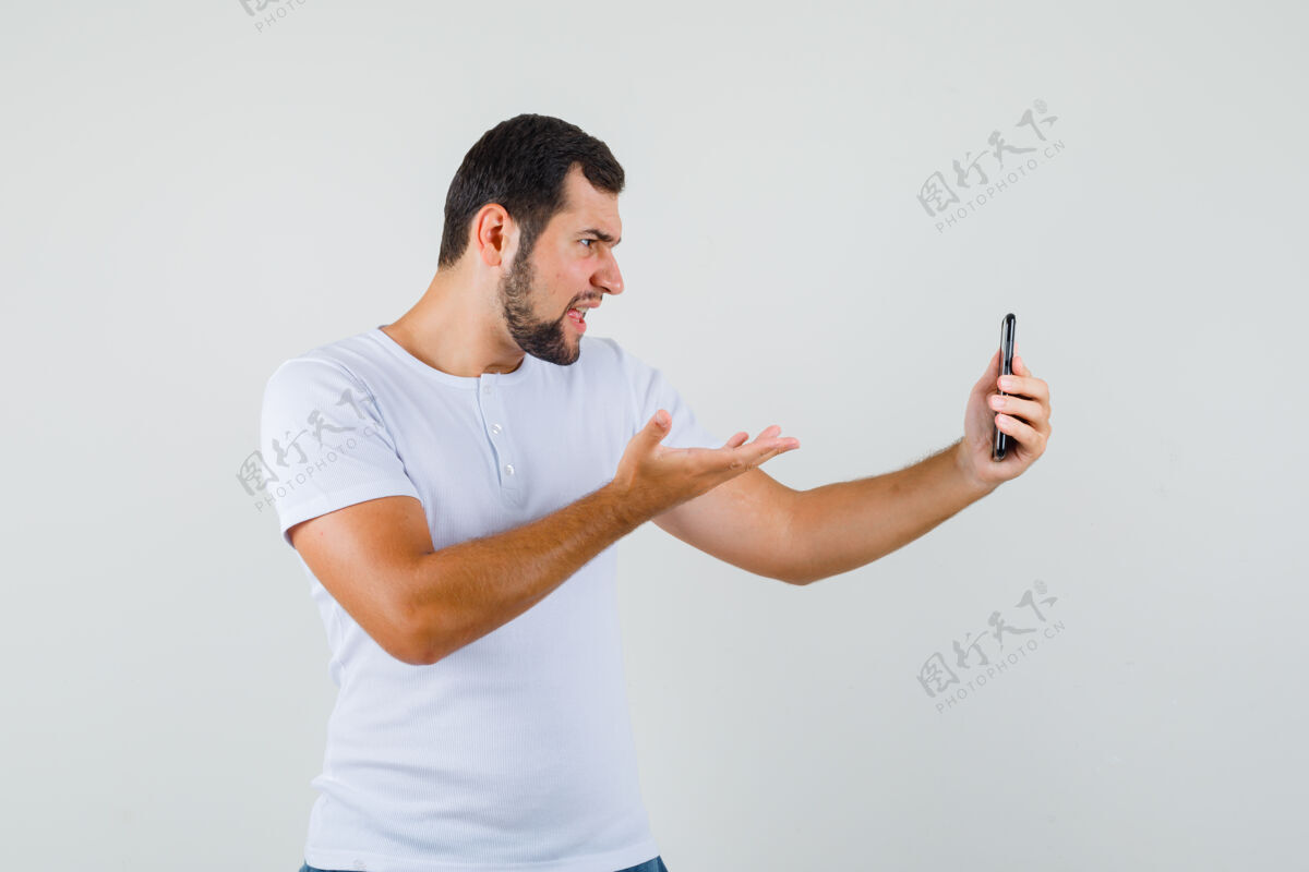 男性一个穿着白色t恤的年轻人在打视频电话时表现出质疑的姿态 看起来很疯狂帅气男人模特