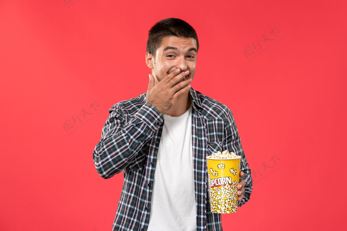 男性正面图年轻男子拿着爆米花包笑着上了淡红墙电影院笑商人电影
