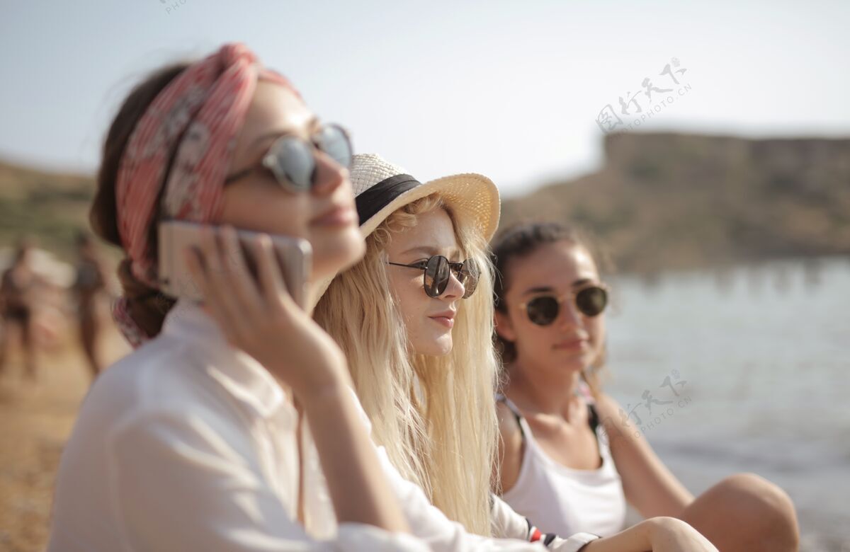 移动三个戴眼镜的年轻女人在沙滩上 一个在打电话人说话现代