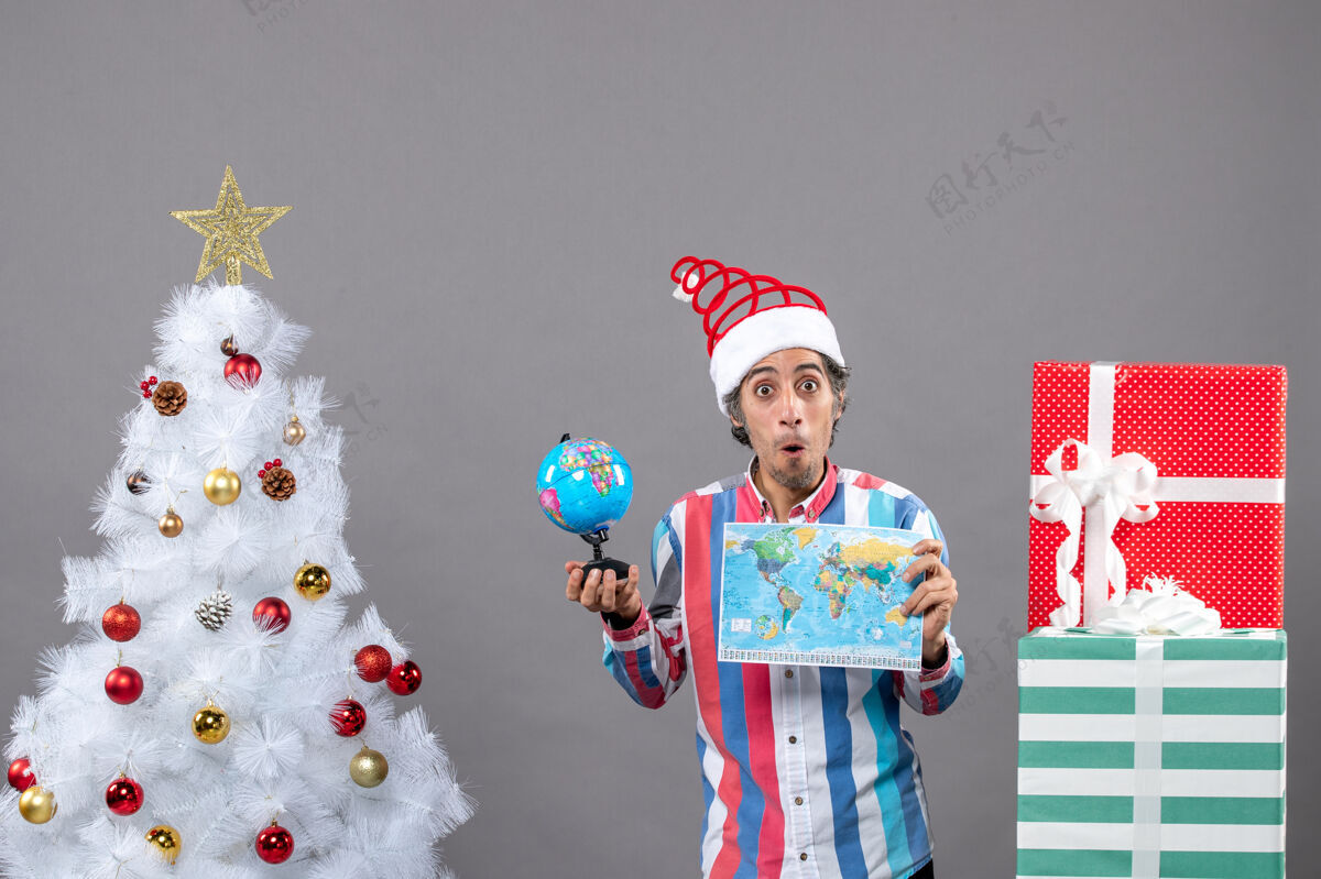 惊喜前视图惊讶的人拿着世界地图和地球仪在圣诞树和礼品盒附近假期人有趣