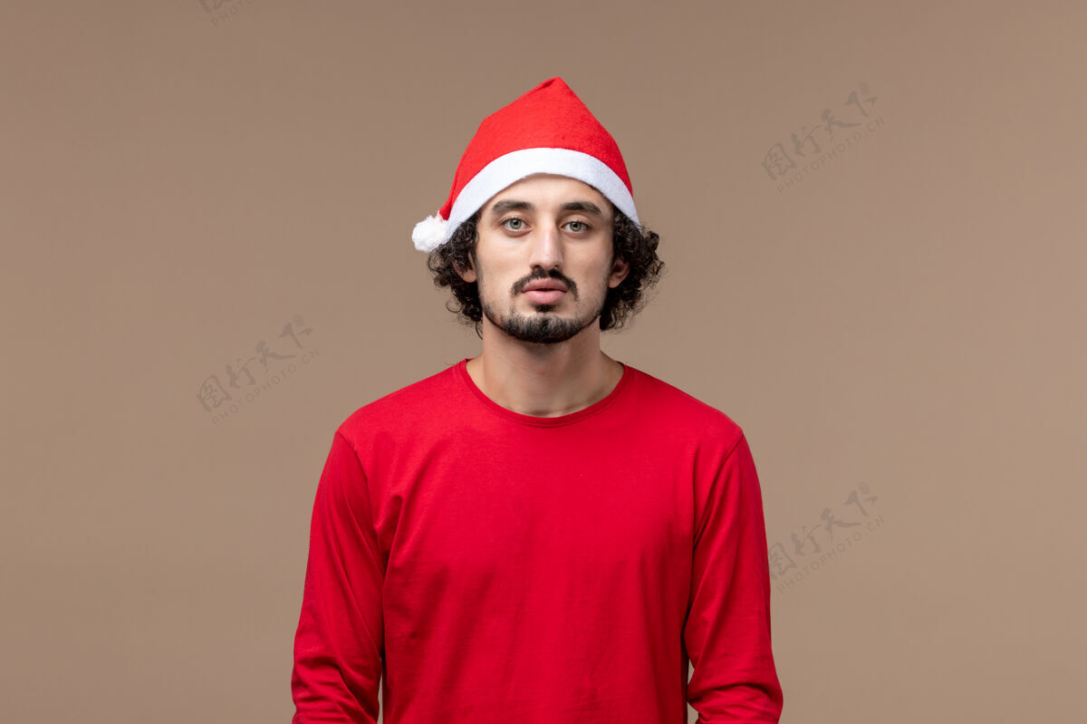 成人正面图：棕色背景上穿着红色圣诞斗篷的年轻男性情感节日圣诞节背景正面工人