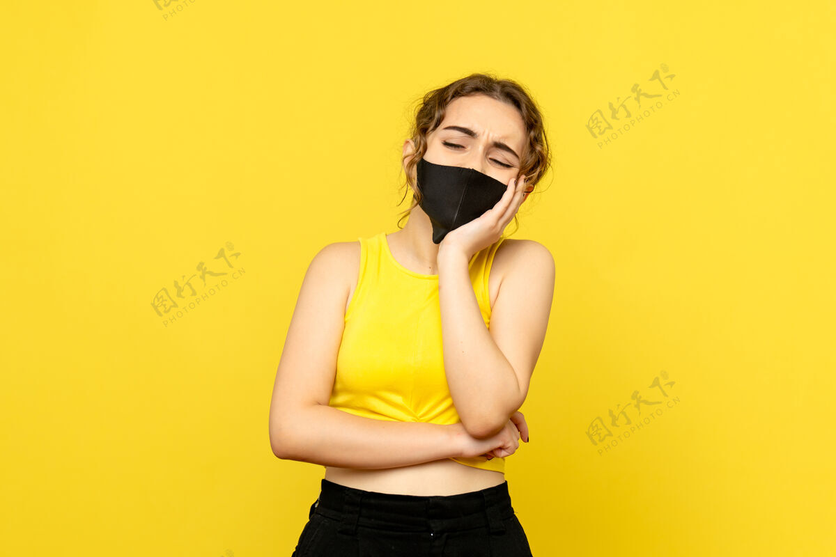 女性黄墙上戴着黑面具的年轻女子的正视图模特时尚面具