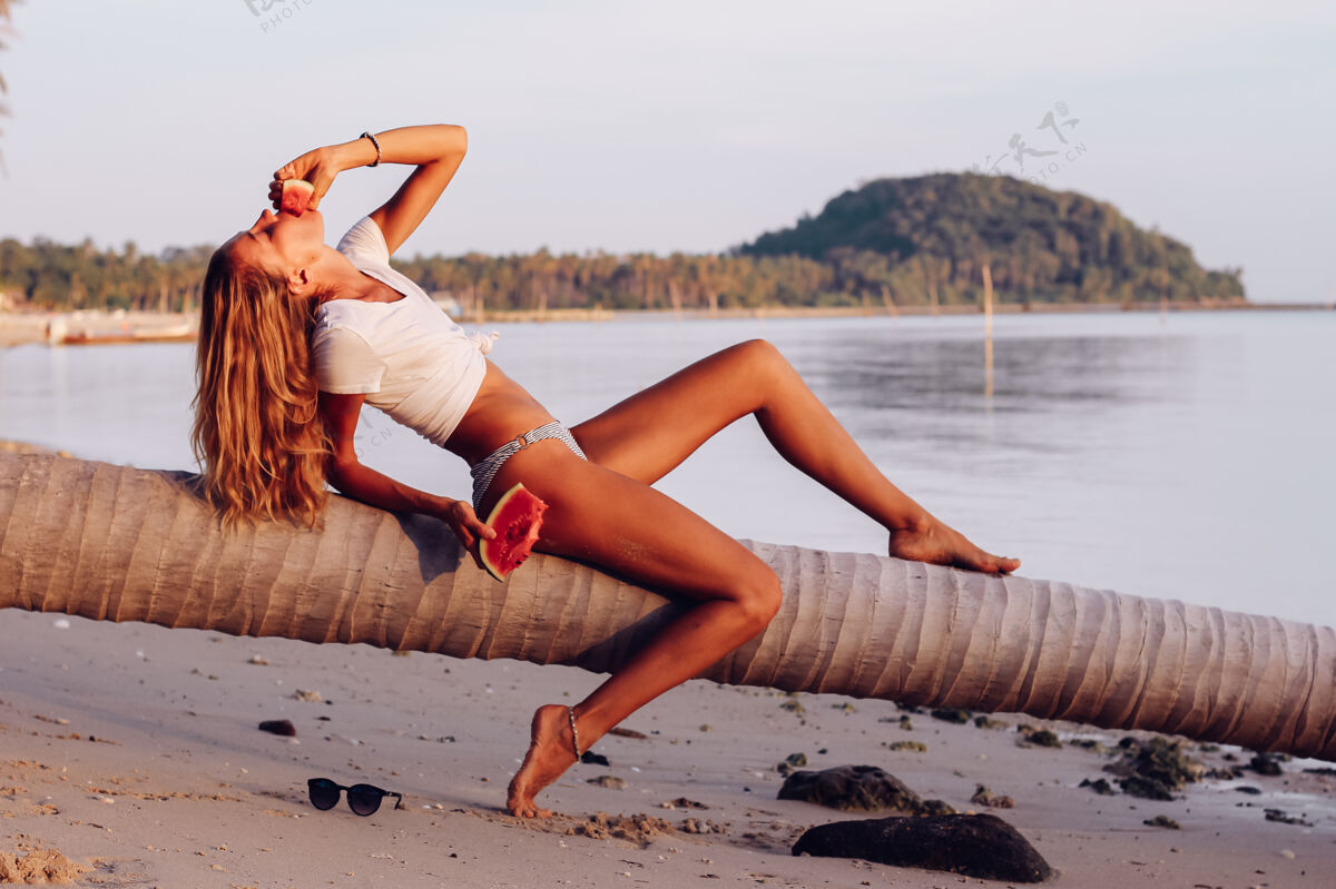 新鲜日落时分 在热带海滩上 一个年轻的女人拿着西瓜美丽热带自然