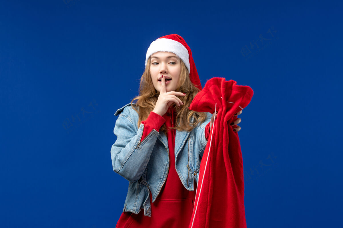 欢快正面图：年轻女性手拿礼物包 蓝色背景 圣诞节情感年轻时尚漂亮