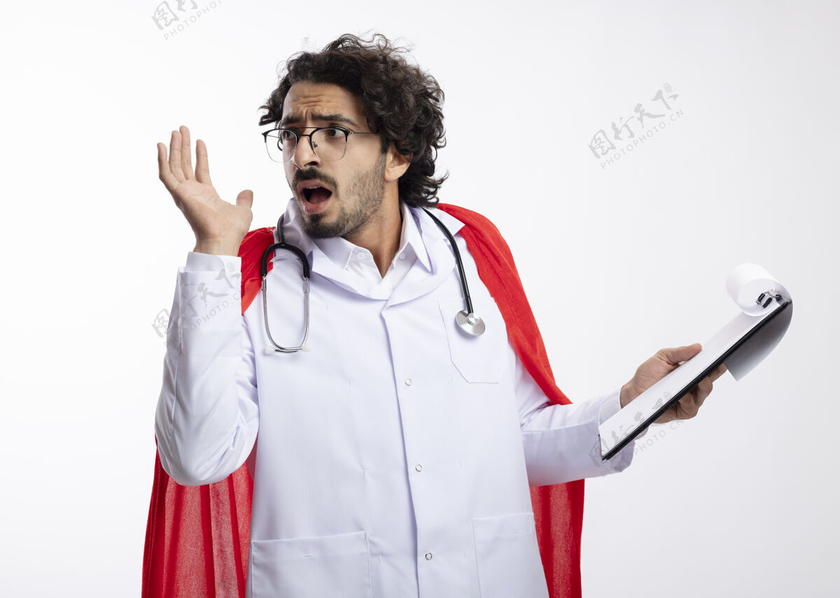 侧面一个戴着眼镜 身穿医生制服 披着红色斗篷 脖子上戴着听诊器的白人男子站起来 举起手拿着剪贴板 看着有复印空间的一边穿着持有光学