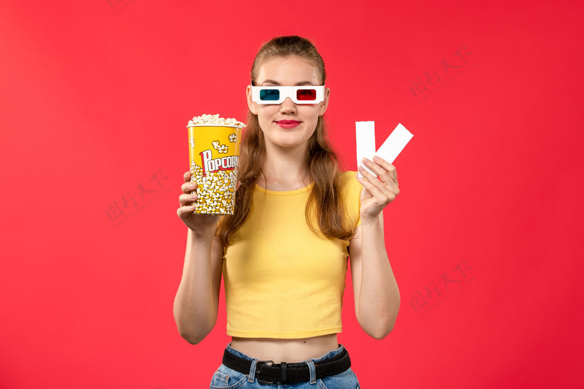 年轻的前视图年轻女性在电影院拿着爆米花包和电影票在淡红墙影院电影票浅红色