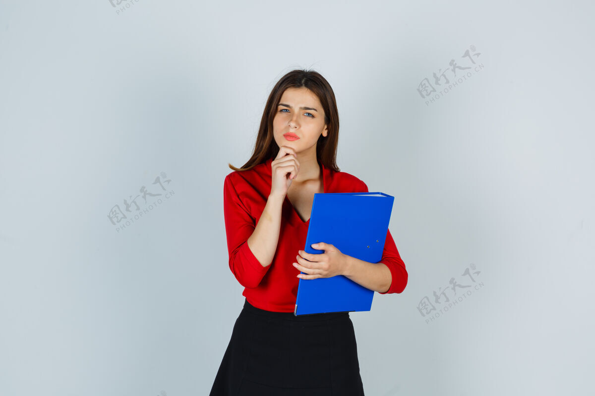 成人年轻女士拿着文件夹站在思考的姿势在红色上衣快乐衬衫文件夹