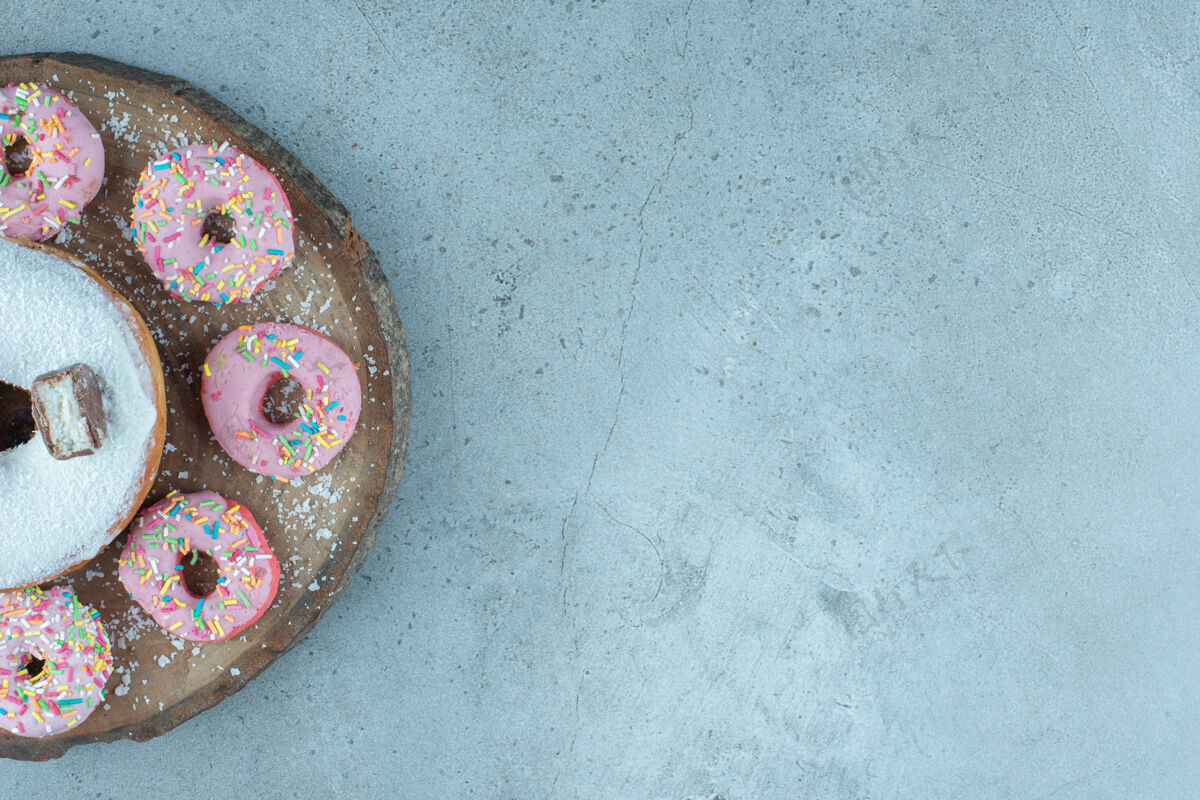 视图小甜甜圈围绕一个大甜甜圈放在大理石木板上烘焙甜点商品