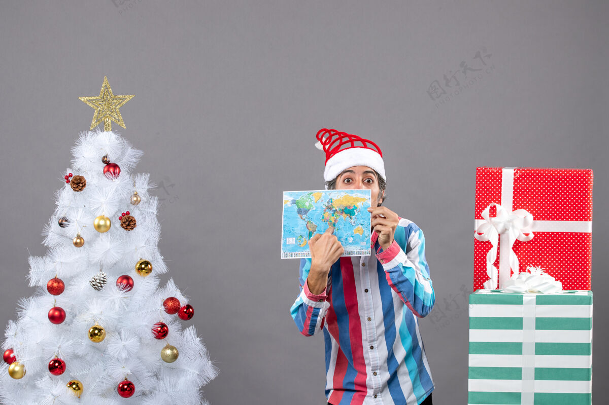 假期前视图惊讶的男子与螺旋弹簧圣诞帽指向世界地图圣诞老人圣诞帽惊喜