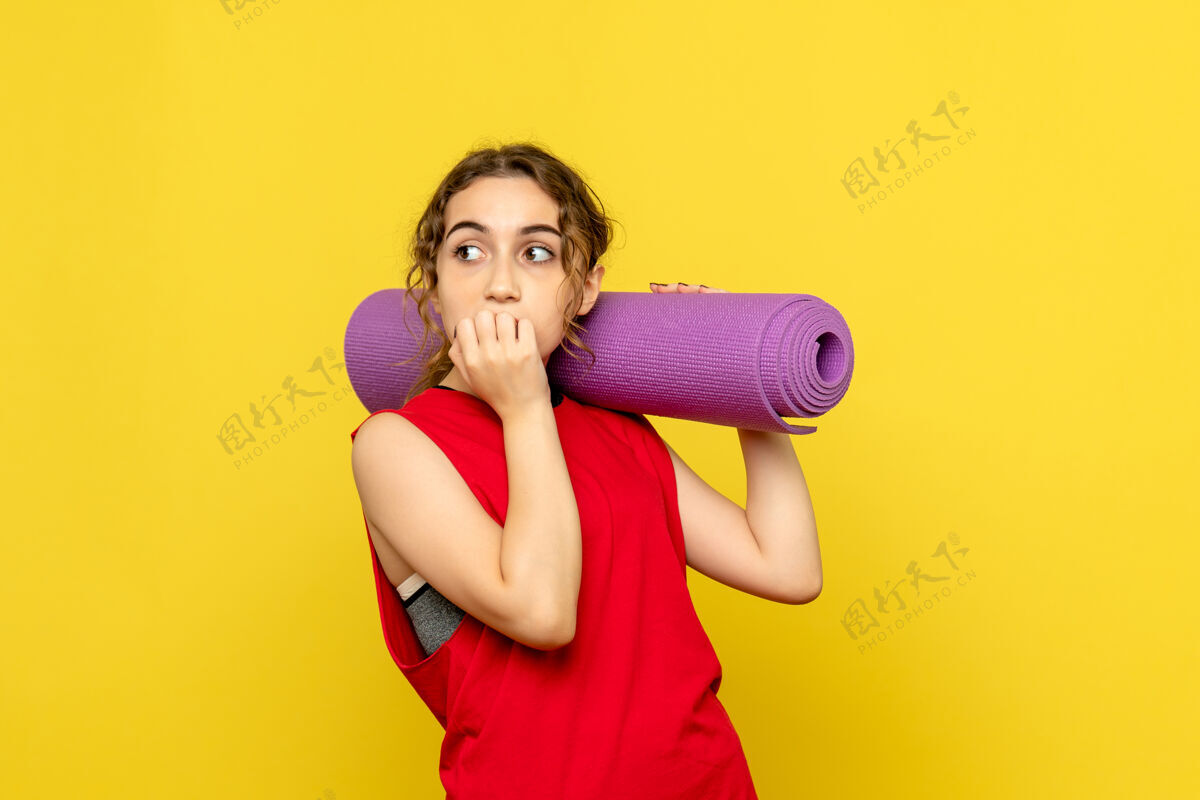 地毯黄色墙上拿着紫色地毯的年轻女子的正视图拳击器械抱着健身