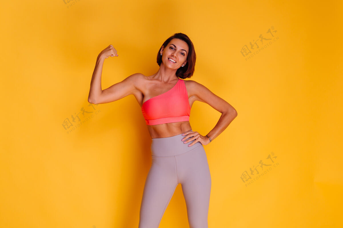 身材年轻健壮的女人穿着运动服 时髦的上衣和紧身裤 对着黄色的墙壁摆姿势运动员健康时尚模特