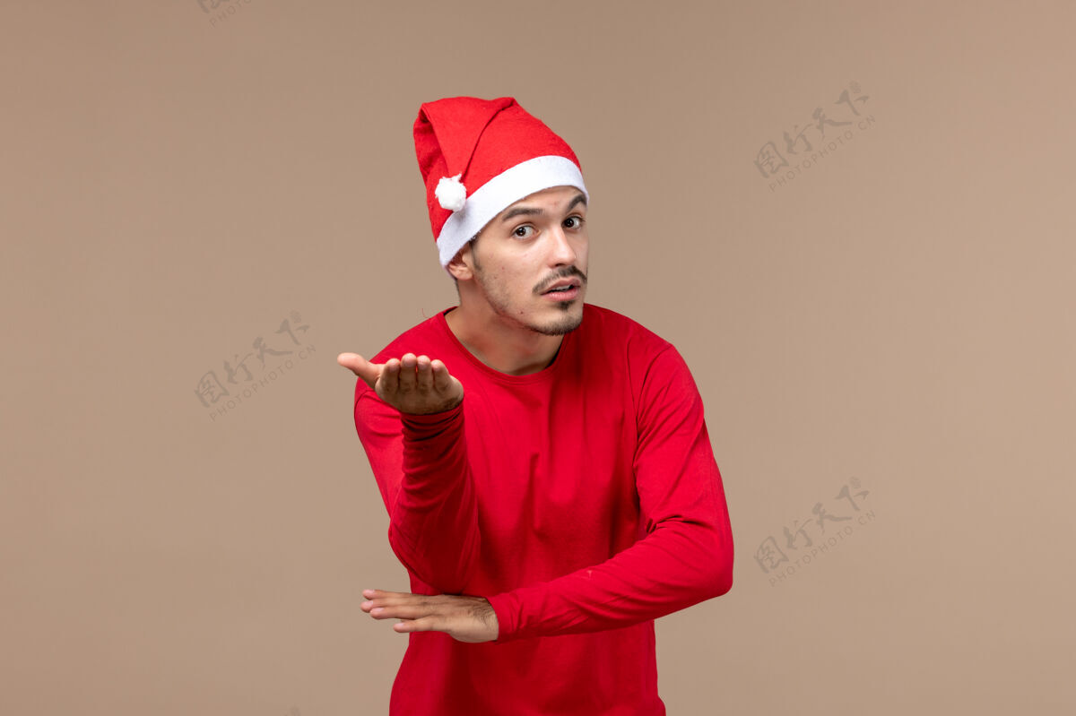 圣诞节正面图棕色背景上困惑的年轻男性圣诞情感节日男性帽子脸困惑