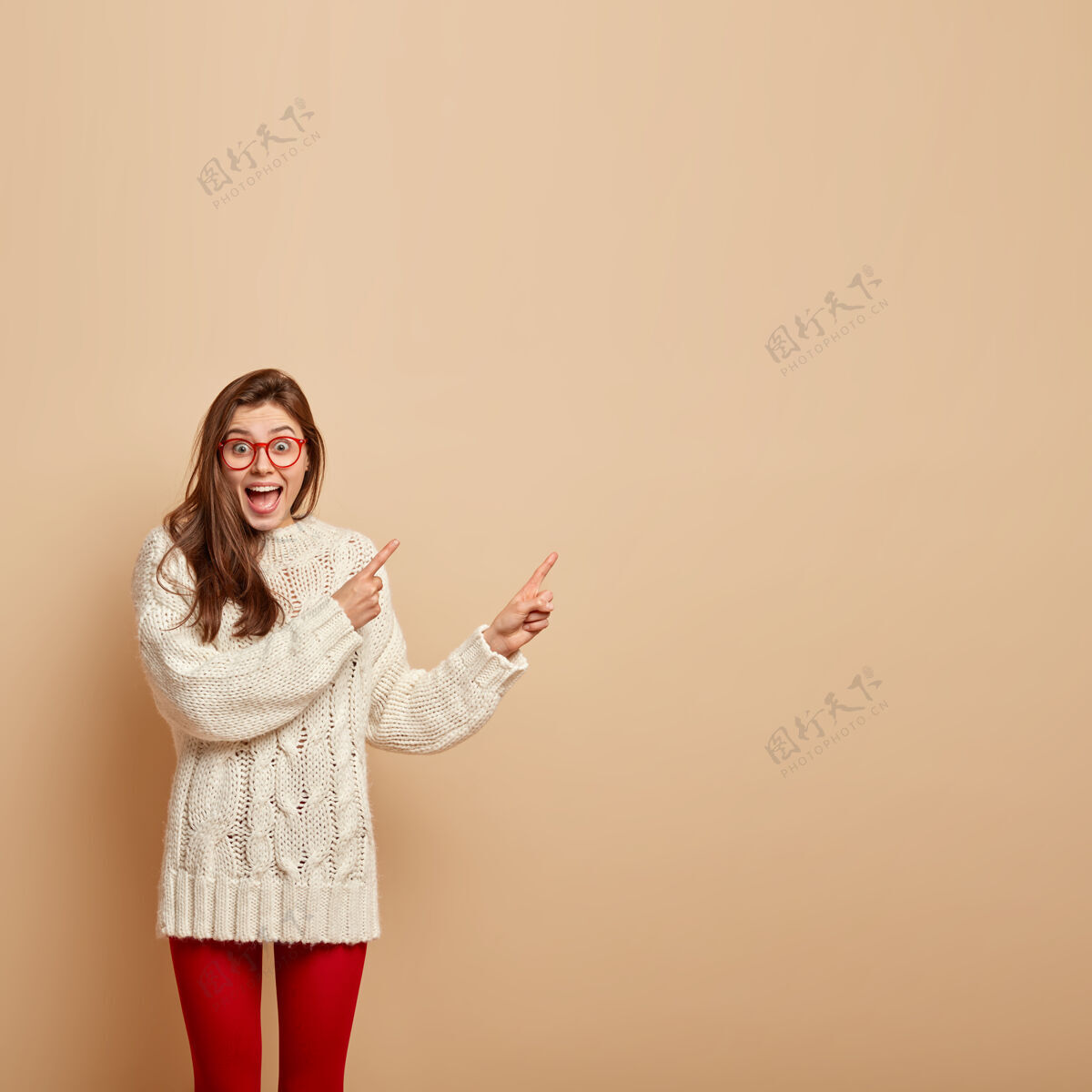 青少年喜怒无常的情绪少女形象 笑逐颜开 指着右上角 宣传酷品 穿白色毛衣 隔着米色的墙休闲满意微笑