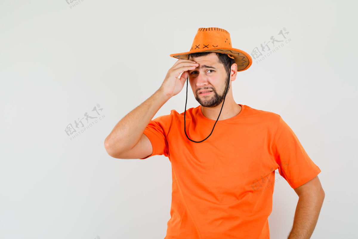 休闲年轻人穿着橙色t恤 戴着帽子 揉着额头 看上去很悲伤前视图男性模特成人