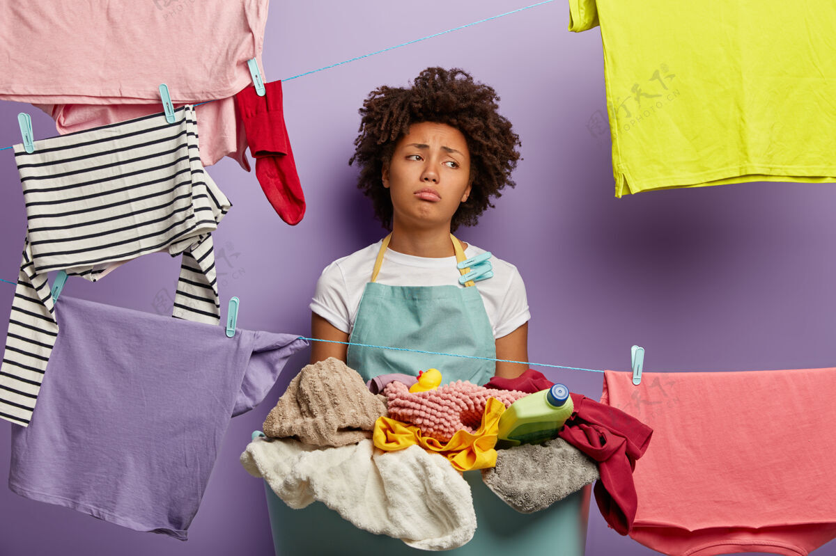 管家家务和洗衣观念不满意的悲伤的年轻女子有非洲发型 用夹子把衣服挂在晾衣绳上 在家洗衣服烦躁悲伤衣服
