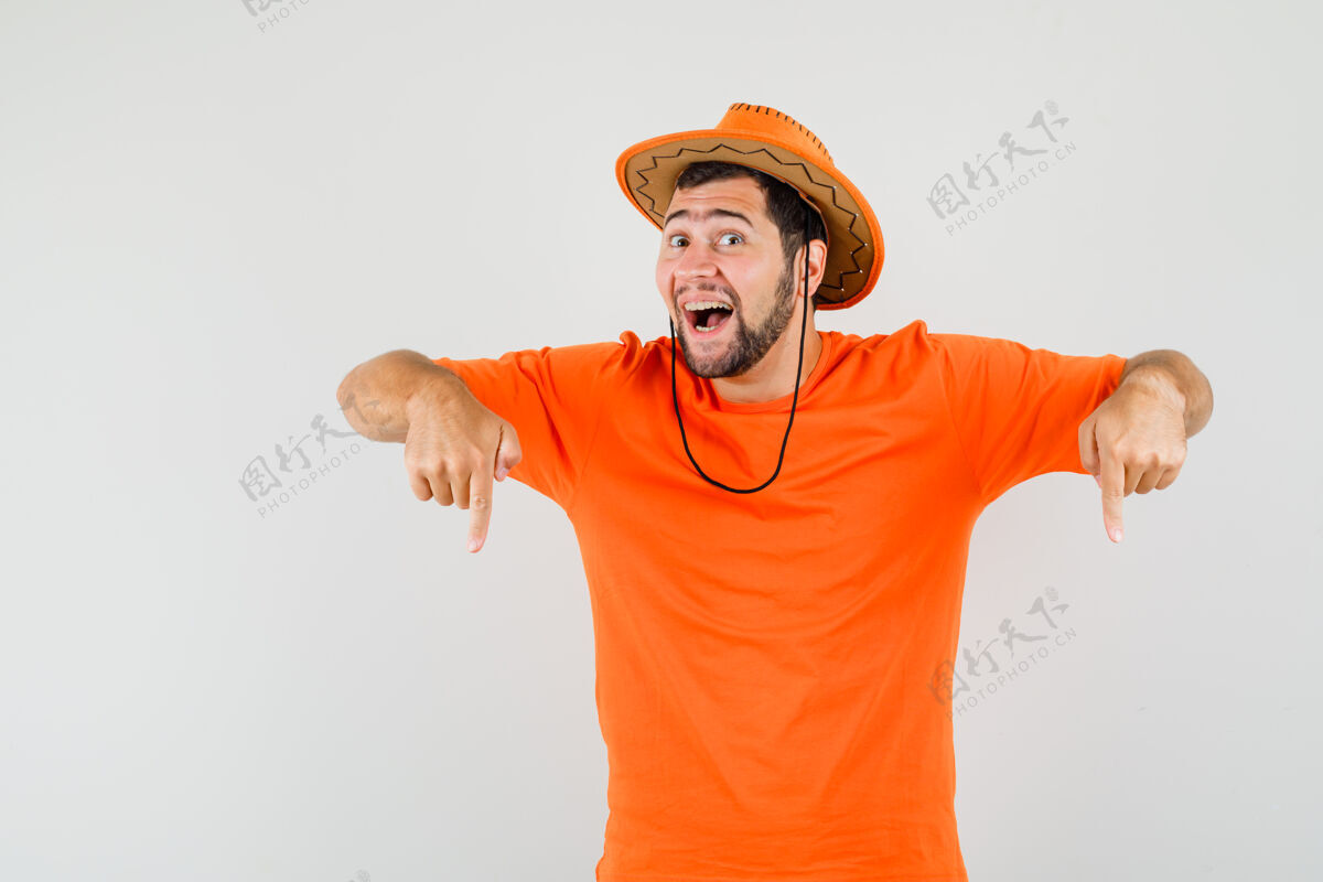 成人年轻人指着手指在橙色的t恤衫 帽子和期待喜悦 正面视图帅气表情人