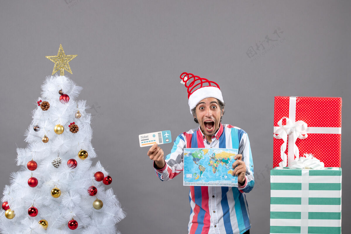 快乐正面图：手持世界地图和旅行票的男人举行圣诞树有趣