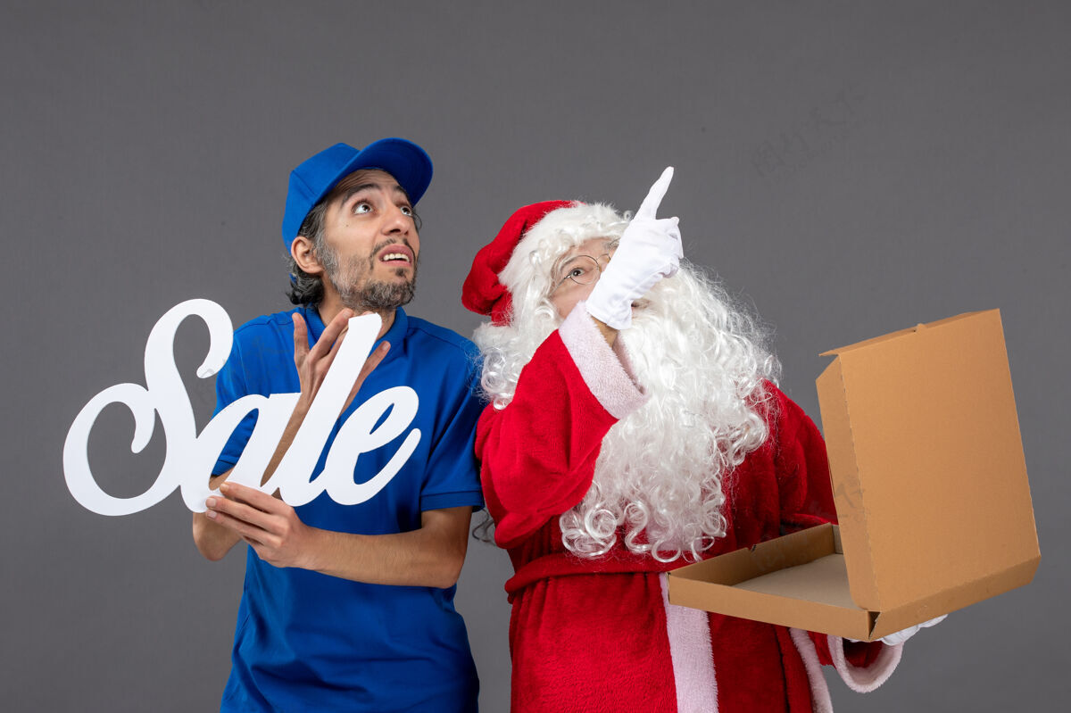 圣诞快乐圣诞老人的正面图 男信使拿着卖东西的字条和灰墙上的食品盒食品举行人