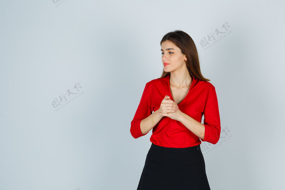 美丽年轻的女士双手紧握在胸前 穿着红色的上衣望着别处休闲商务沉思